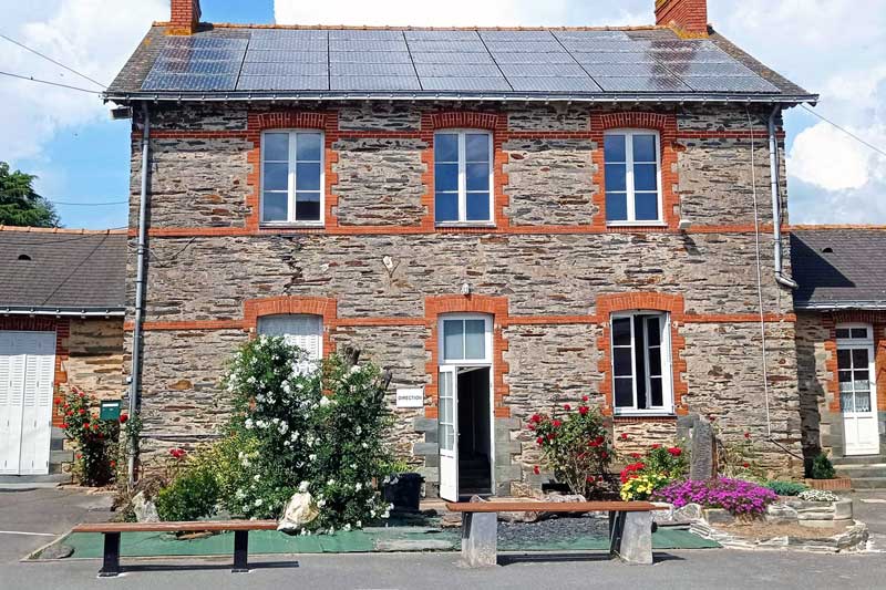 Le bâtiment administratif du Collège Saint Joseph de Nozay en briques et pierres, accompagné de son parterre de fleurs colorées.